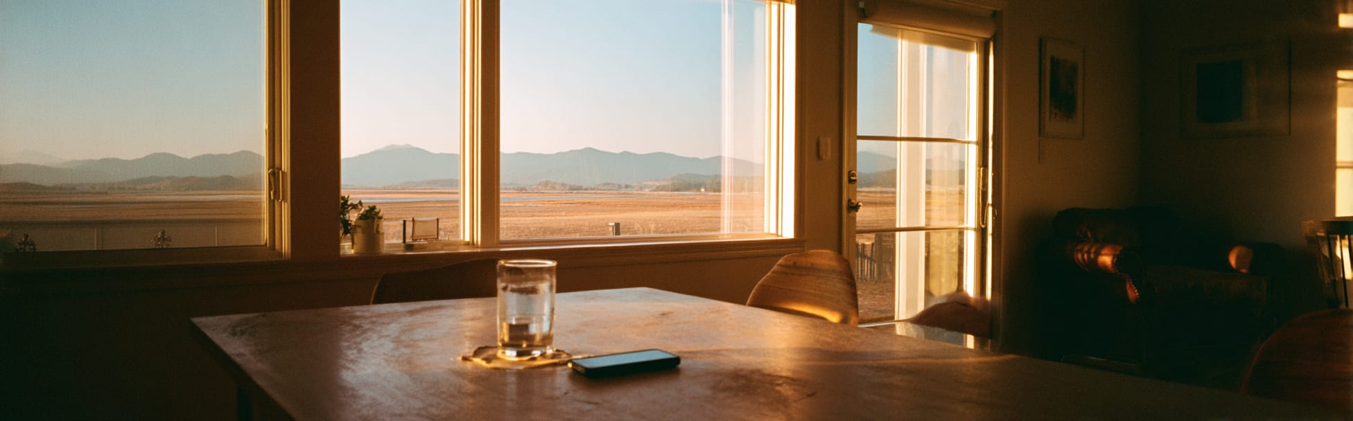 Luz de la mañana por la ventana de una cocina, un vaso de agua y un teléfono sobre la mesa